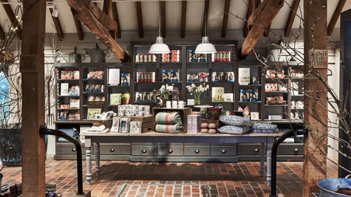 Inside the shop, with a display table piled with blankets, cushions and other products, at Sissinghurst Castle Garden, Kent